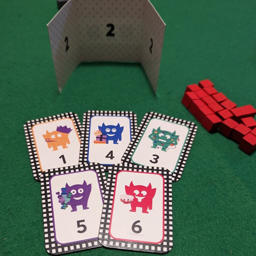 playing cards with imps on, some red cubes and a card folded to provide a barrier. One of the christmas cracker games